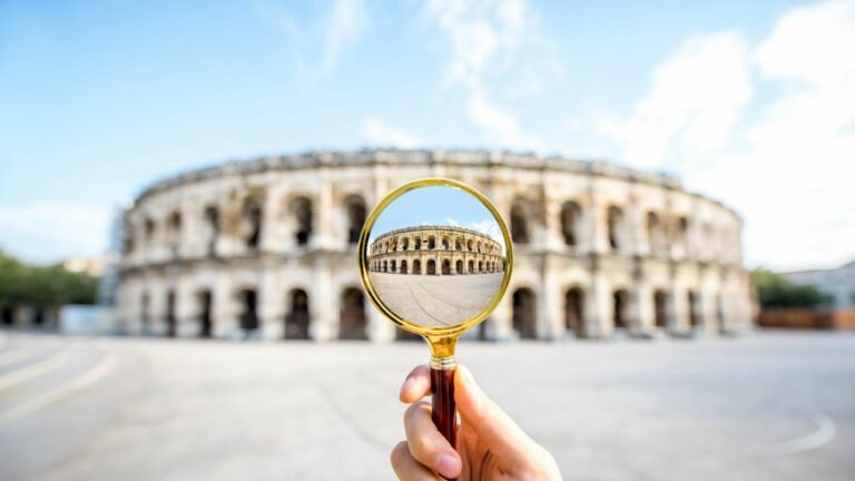 Main tenant une loupe devant les arènes de Nîmes pour en révéler les détails.