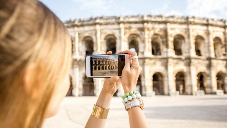 Femme photographiant les arènes de Nîmes avec son smartphone.